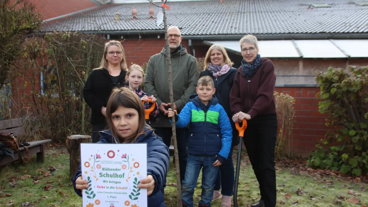 Auf dem Bild sind die Kinder und Erwachsenen beim Baumpflanzen zu sehen.
